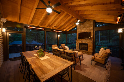 Inside of a screened porch that has a stone fireplace. While talking about Thinking about adding a new deck or porch to your home? You might be wondering how the 2025 tariffs could affect your project’s cost.